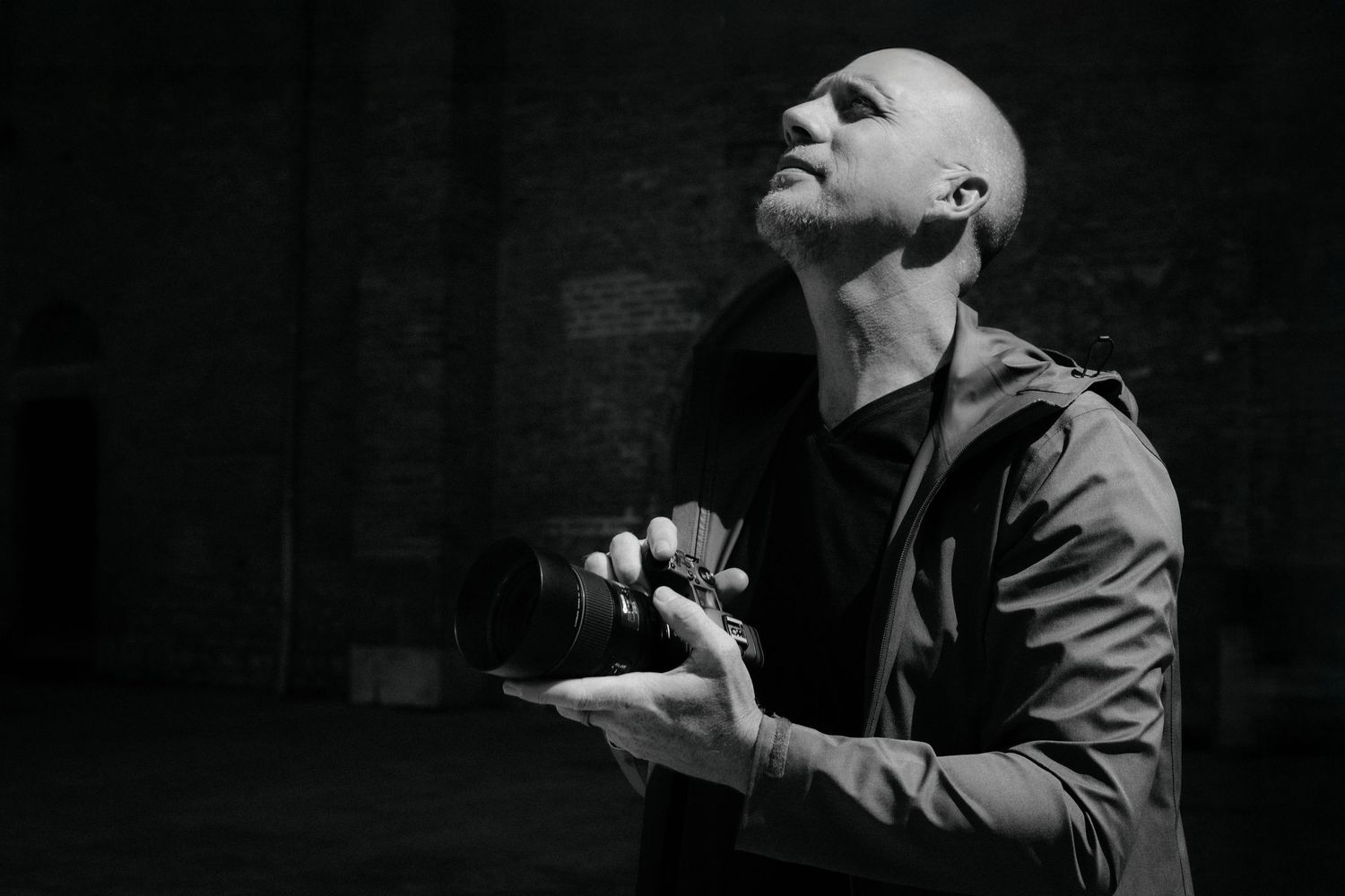 A person in a dark setting looks upward with dramatic lighting creating a moody silhouette effect.