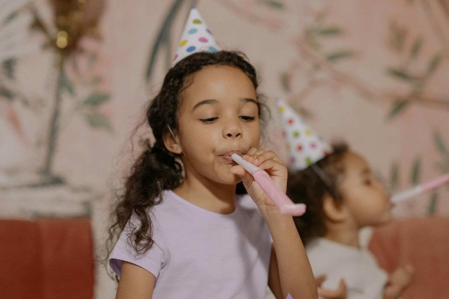 young girl with a birthday hat on blowing a noice maker as she celebrates a birthday party