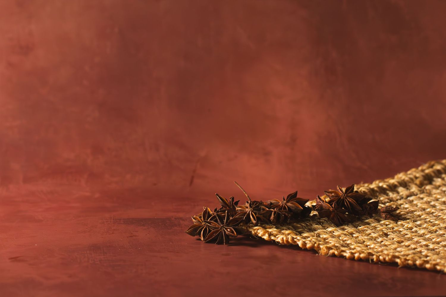 Star anise spices scattered on burlap fabric against a rich dark red background. B. Steele Images, food & beverage photography
