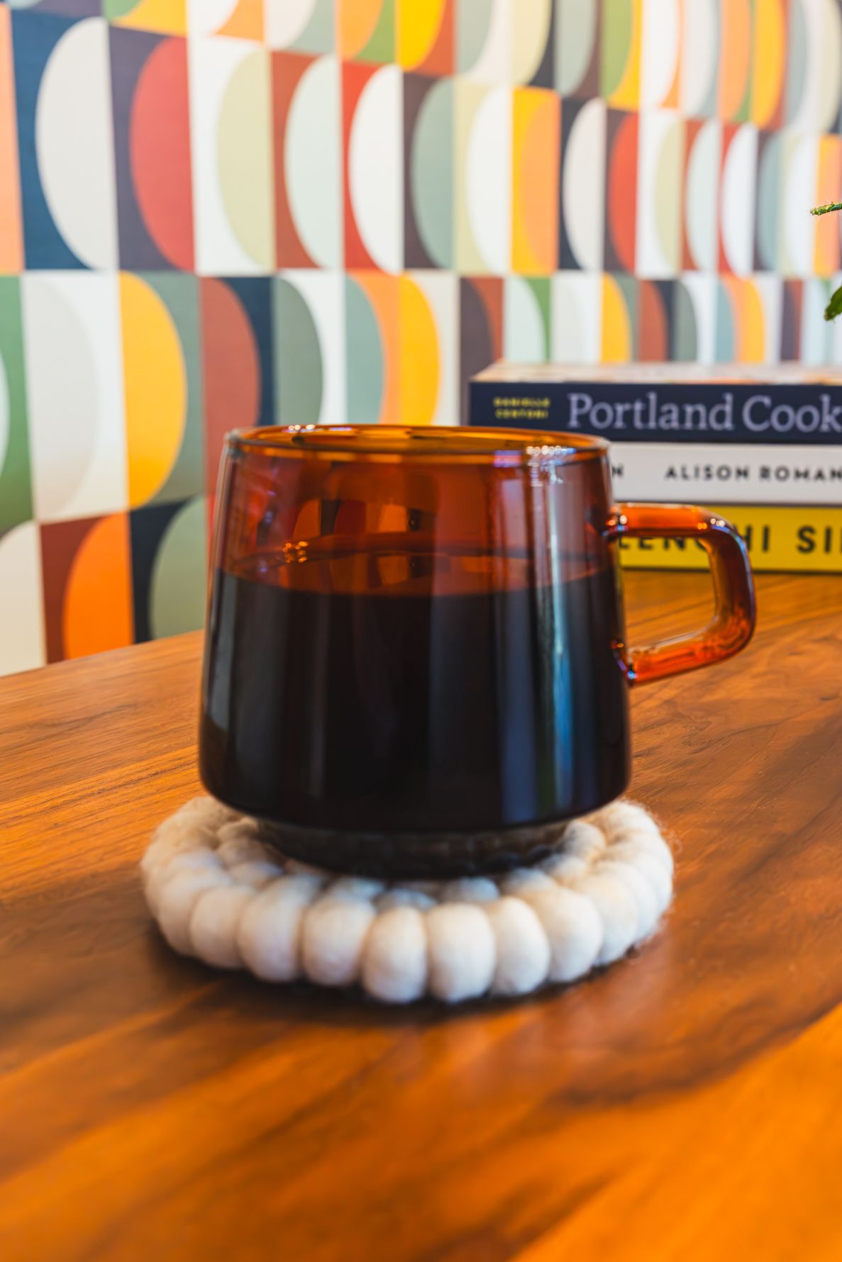 Amber glass mug filled with black coffee on a white coaster, beside Portland Cookbook on a wooden table. B. Steele Images, photography