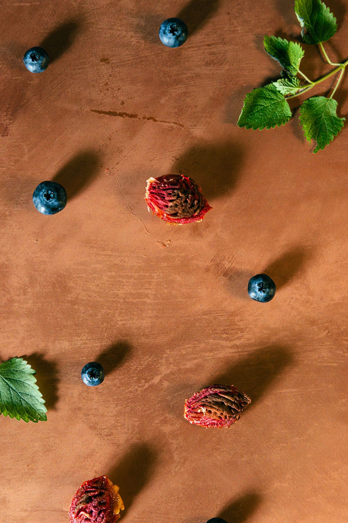 Fresh blueberries and peach pits scattered on a rustic brown wooden surface with basil leaves. b. steele images