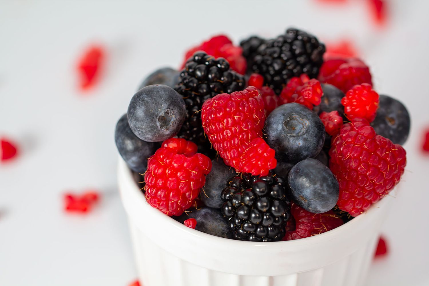 Fresh mixed berries including raspberries, blueberries and blackberries in a white ceramic ramekin on light background. Brigit Steele photo