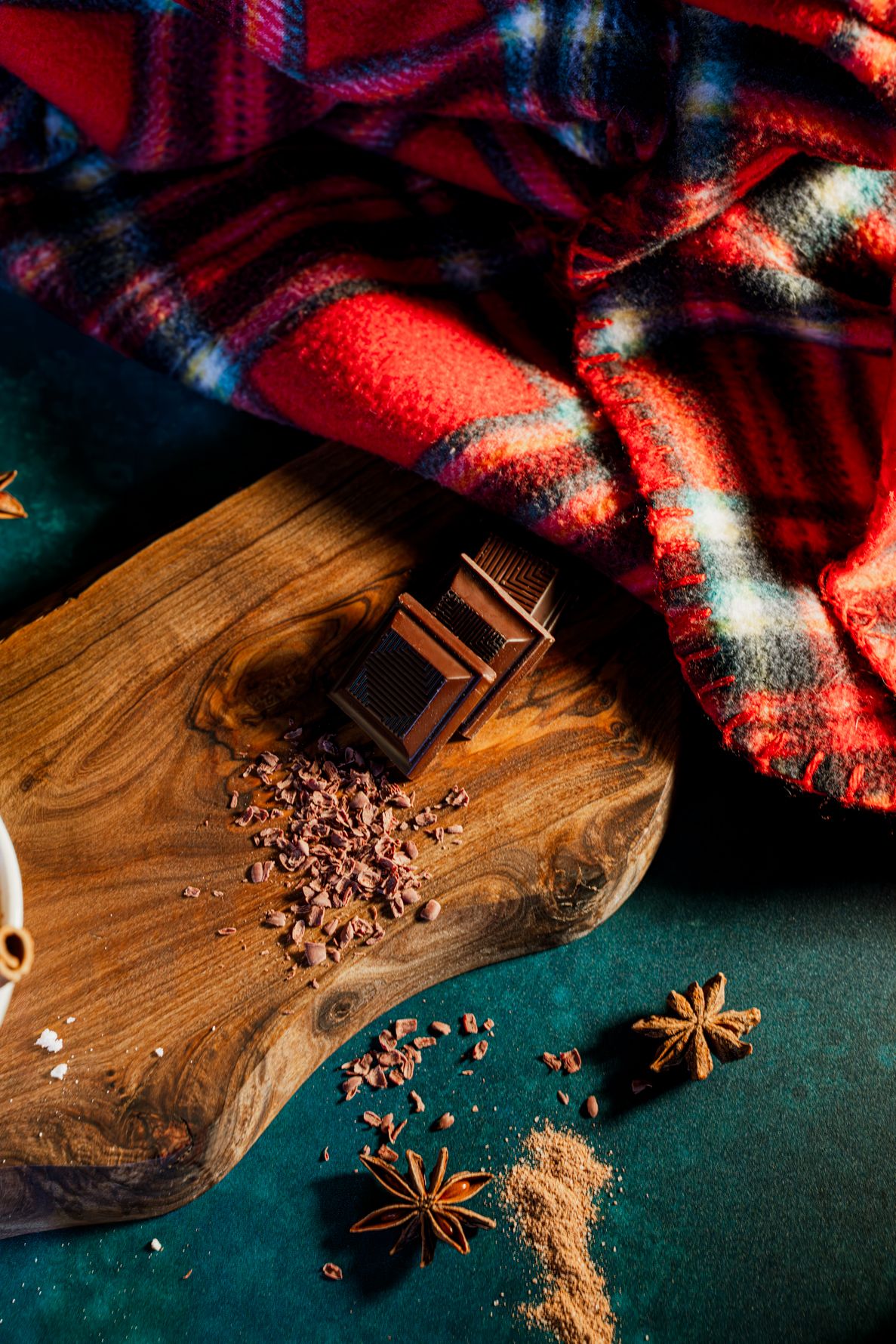 Shaved chocolate, chocolate scares and star anise on a rustic wooden cutting board with a cozy plaid blanket in red lighting. B. Steele Phot