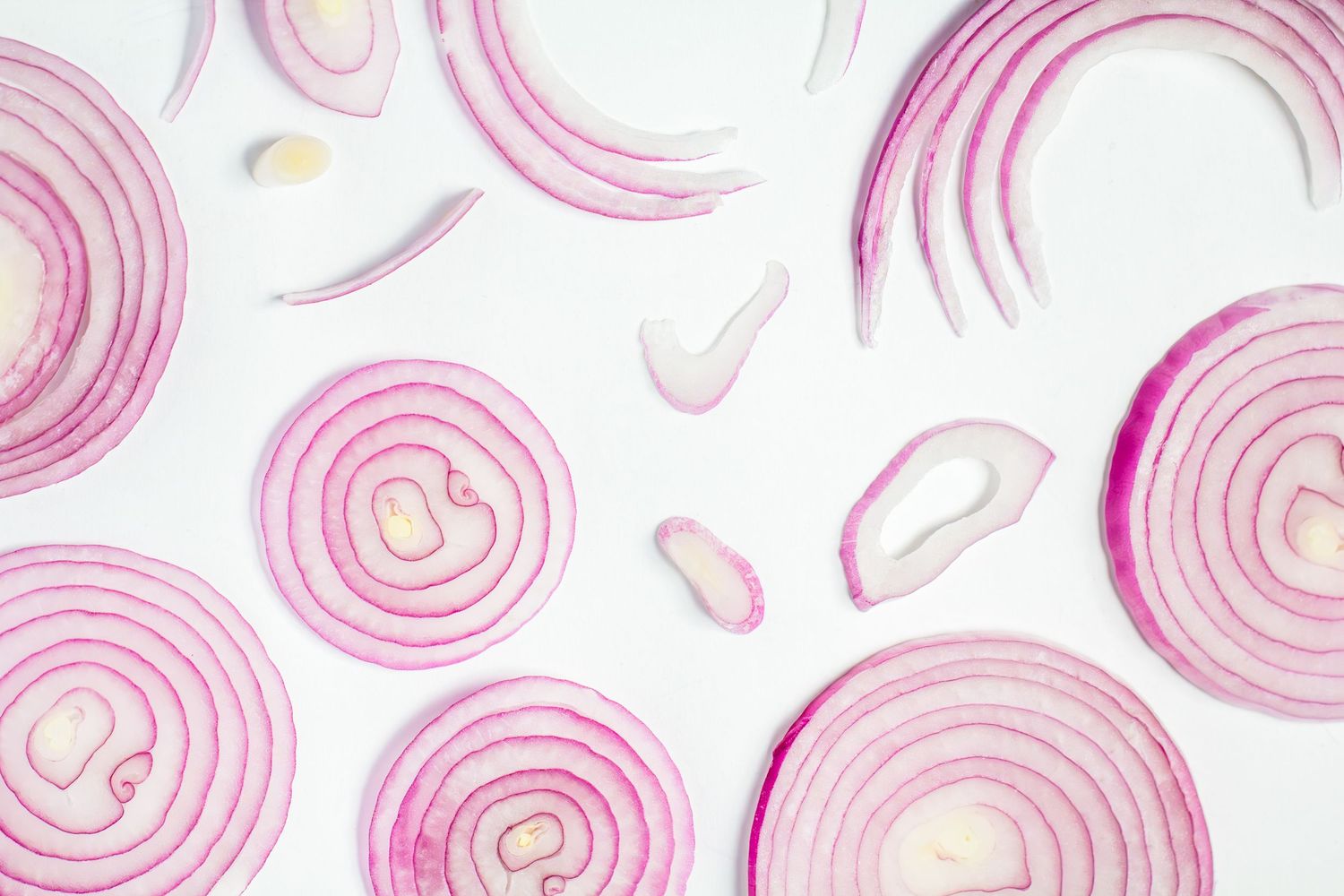 Sliced red onion rings arranged in a pattern on a white background creating a delicate pink circular design. B. Steele Images, food photos