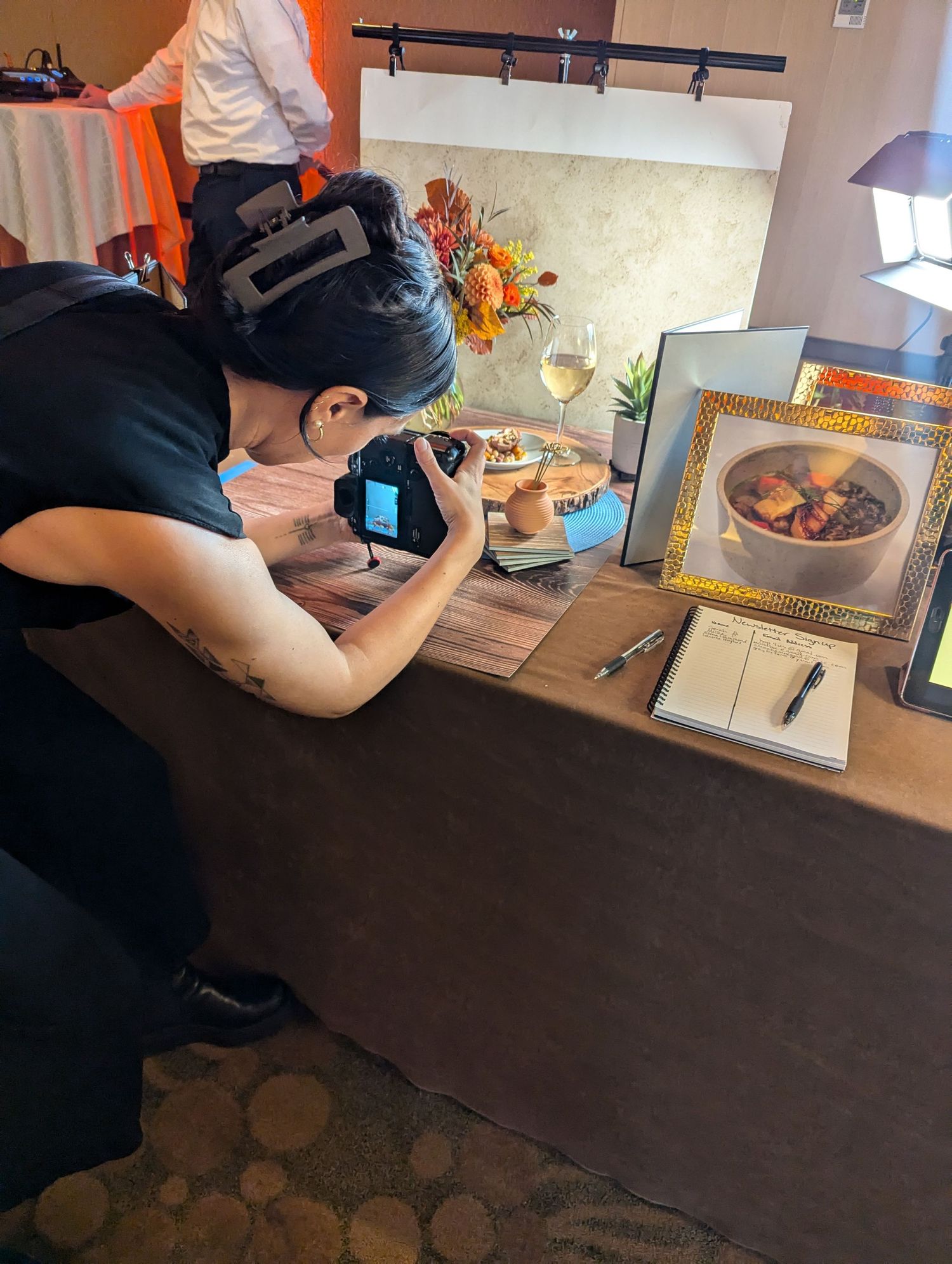 Photographer with camera leans over table taking close-up shots of food dishes in a scene built for educating photography