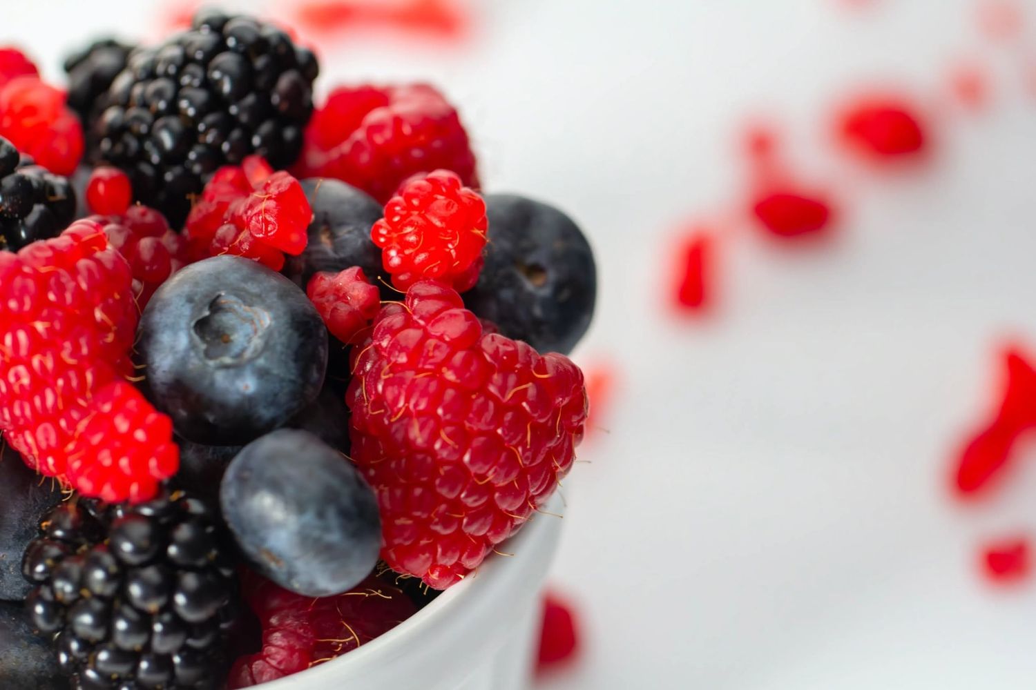 Fresh mixed berries including raspberries, blackberries and blueberries scattered on a light surface. B. Steele Images, Portland, Oregon.