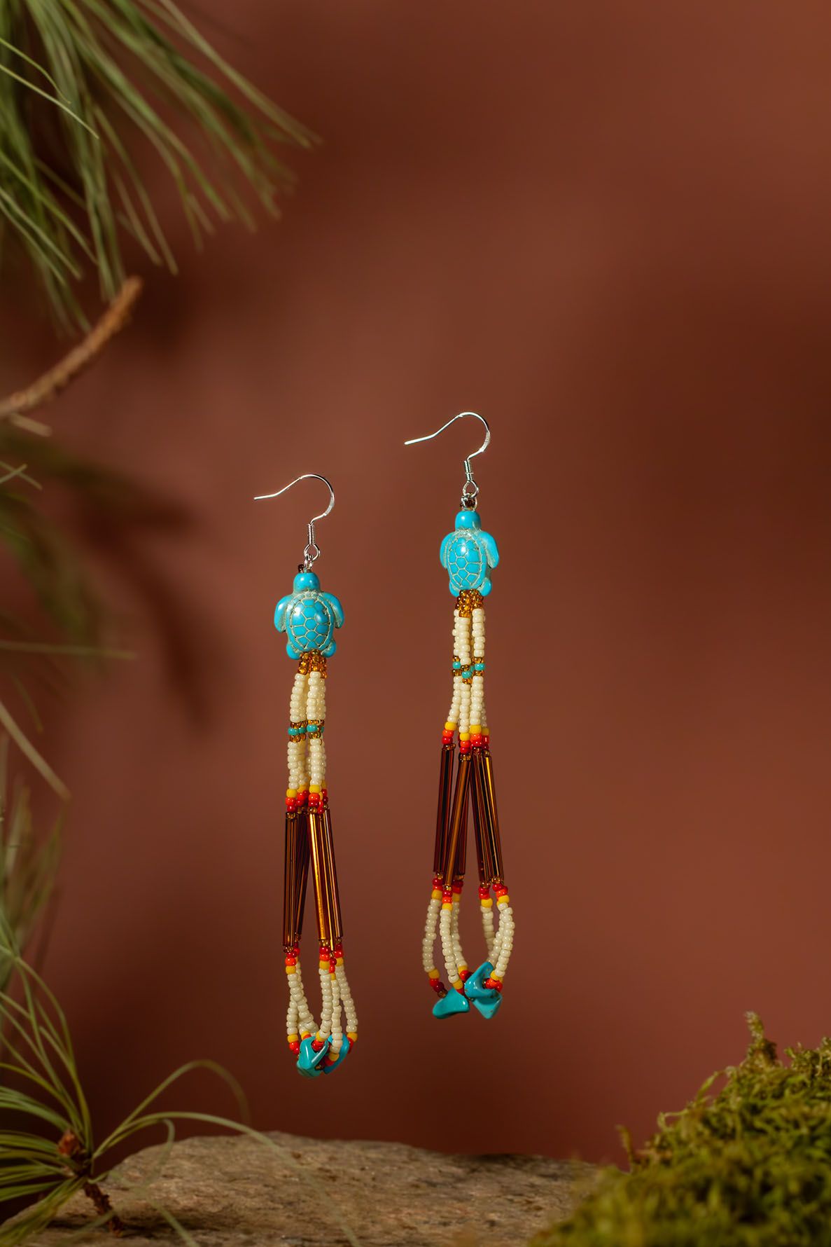 Handcrafted turquoise and amber beaded Native American style earrings shown in earthy scenery against a brown background.
