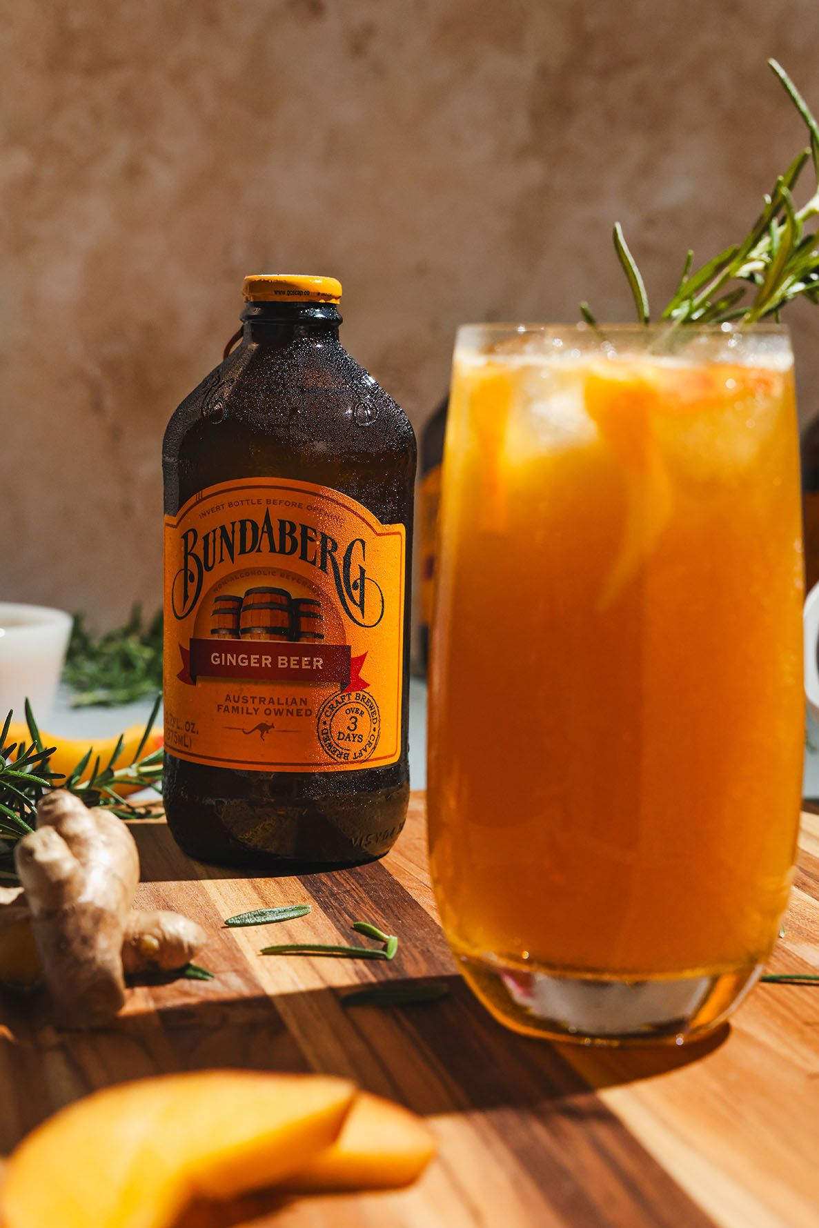 Orange Bundaberg mocktail garnished with fresh rosemary sprig served in a coupe glass on wooden surface with bottle in background.