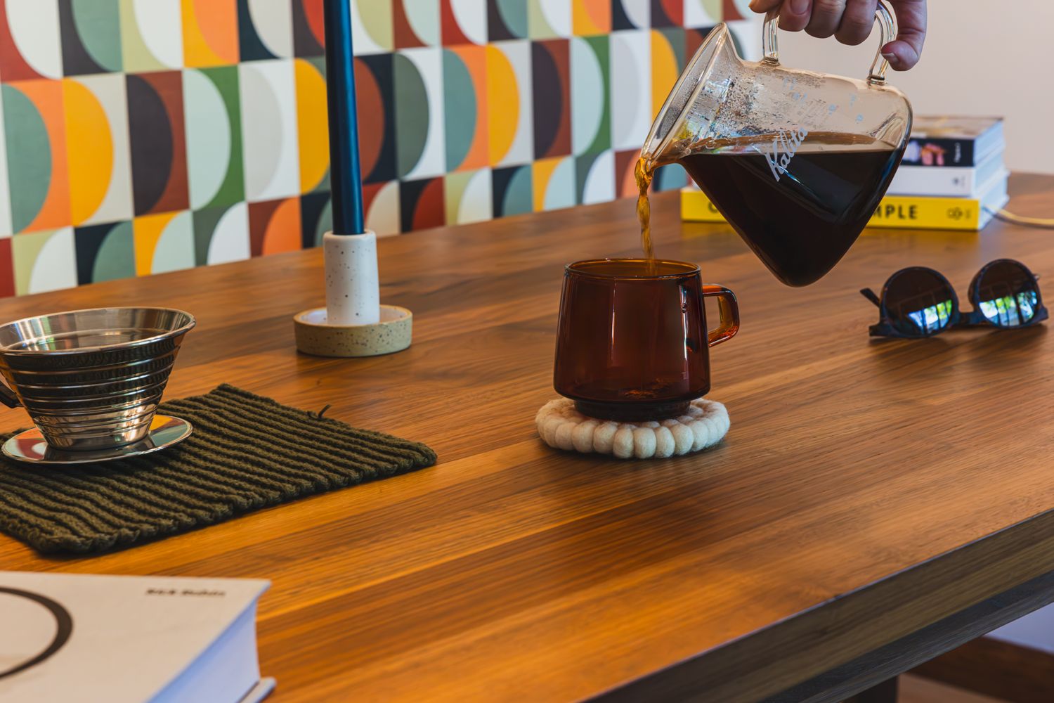 Modern wooden desk with Chemex coffee maker, books, and colorful geometric wallpaper in a stylish home office setting. b. steele images