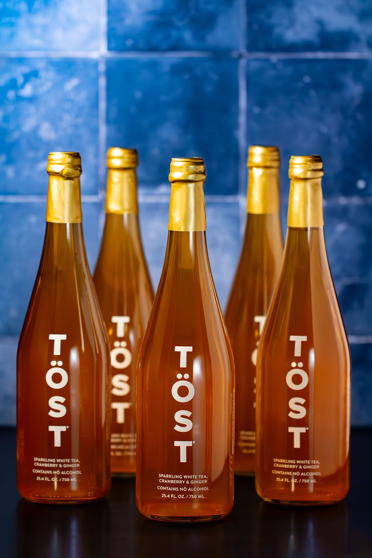 Amber glass bottles with minimalist Tost lettering arranged in a row against a dark blue background. Beverage styling, photography.