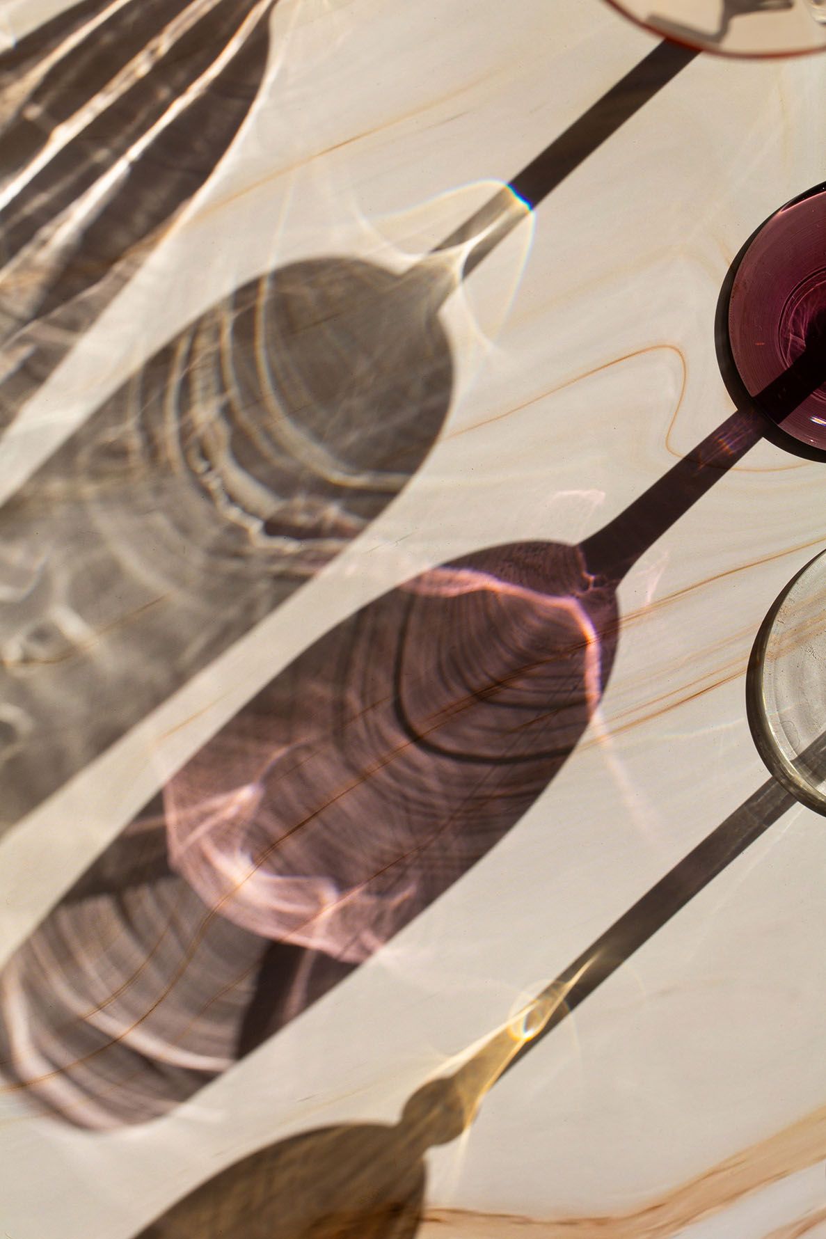 A sequence of images showing sunlight casting shadows through wine glasses, creating artistic reflections and patterns. B. Steele Images