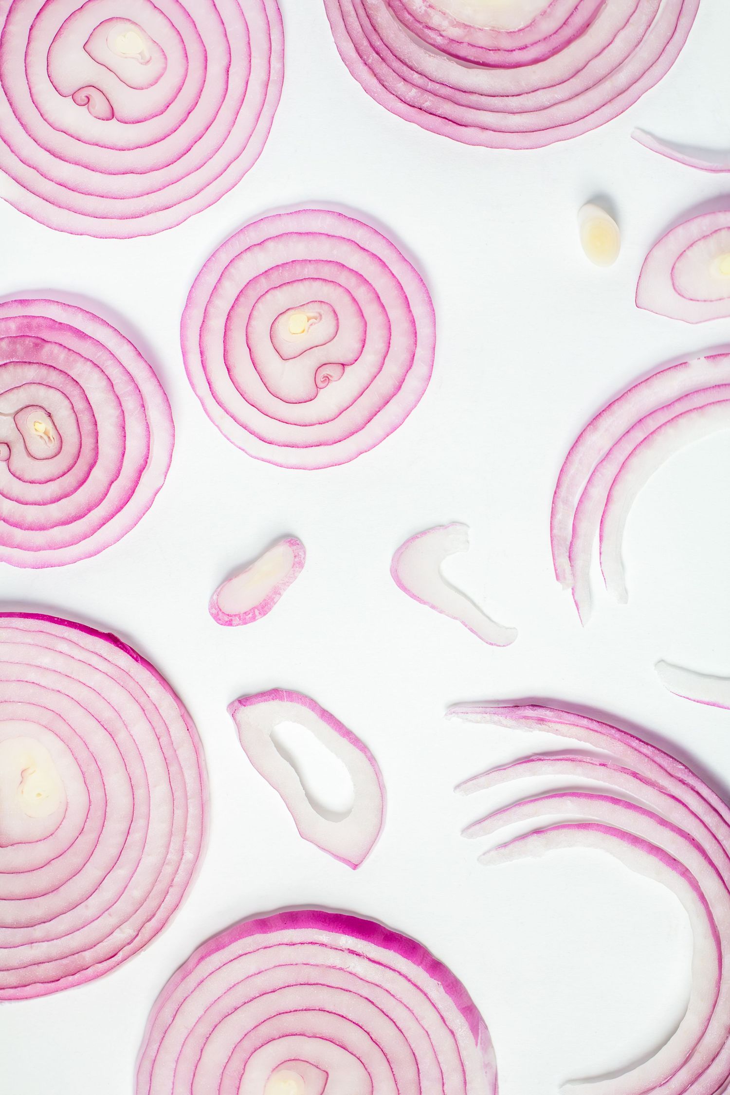 Sliced red onion rings arranged in a pattern on a white background creating a delicate pink circular design.