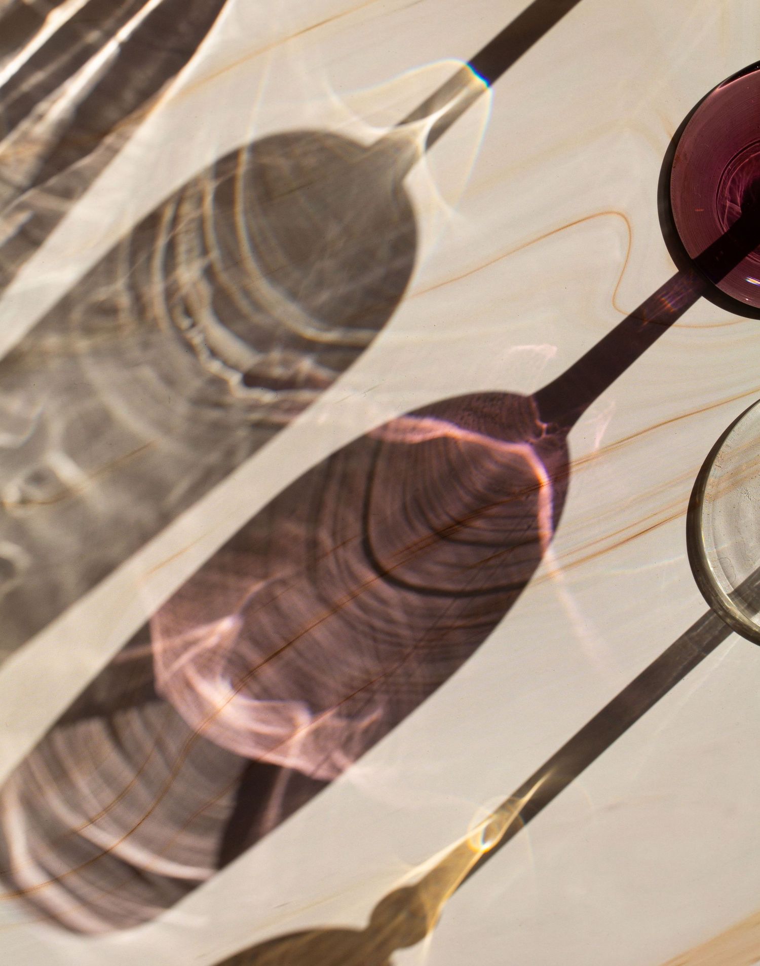 A series of wine glasses casting long shadows on a white surface creates an artistic diagonal pattern.