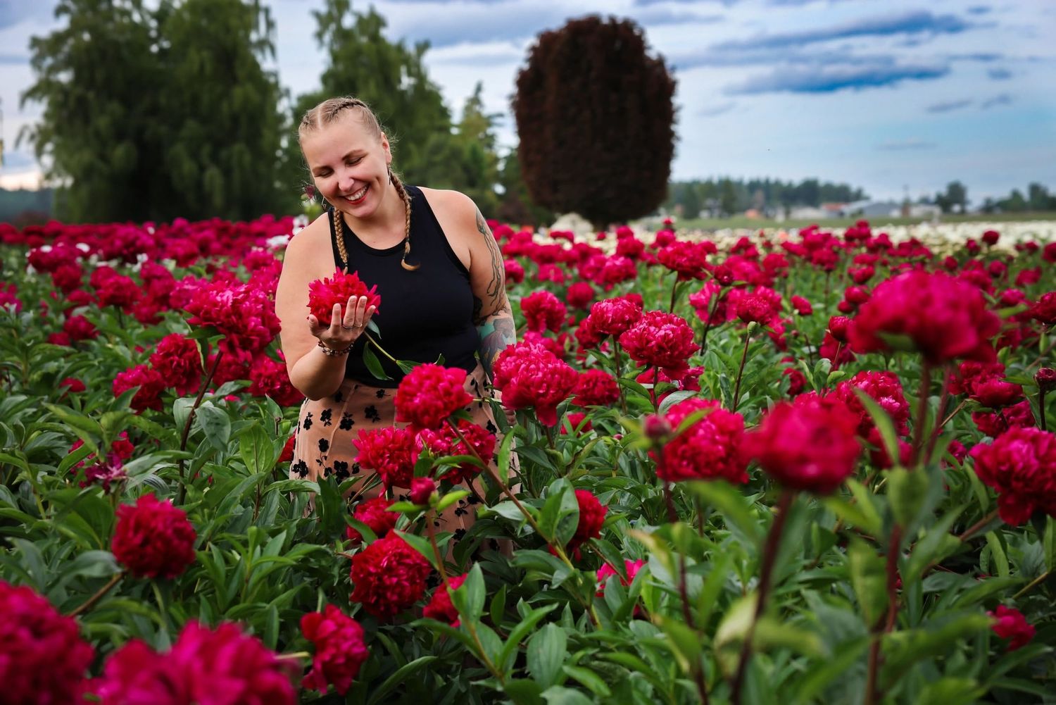 Photographer Brigit Steele smiles while standing in a vibrant field of red flowers on a sunny Pacific Northwest day.