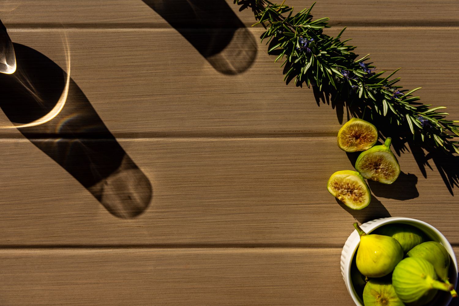 Fresh green figs and a glass jar cast dramatic shadows on a rustic wooden table surface. B. Steele Images, food and beverage photography
