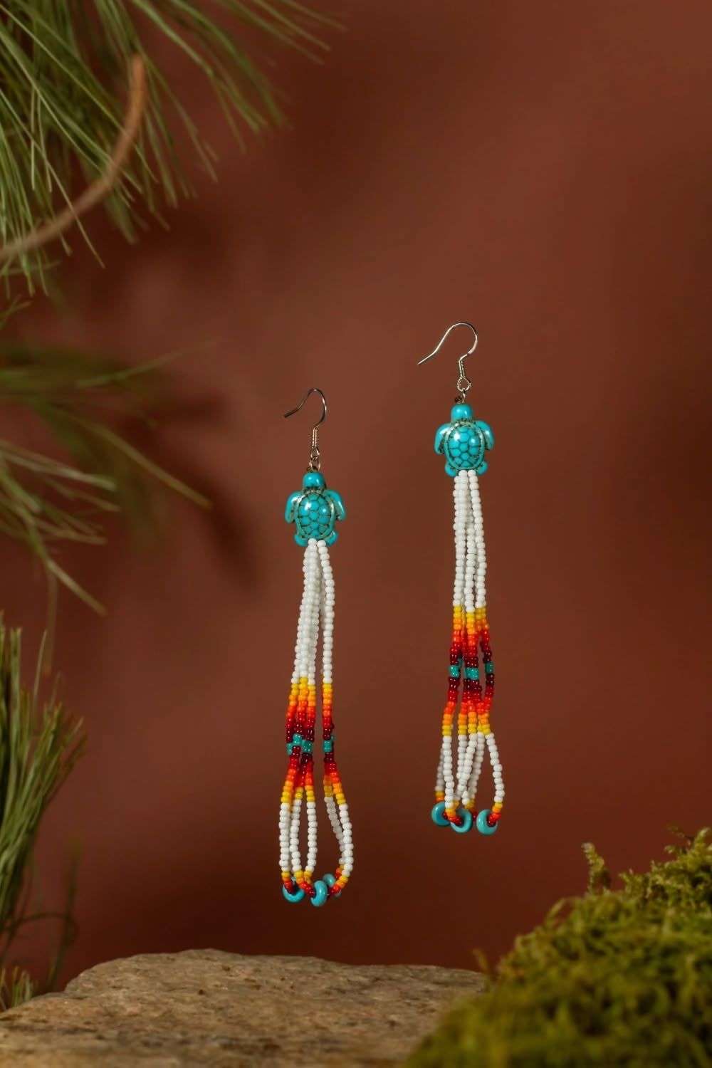 Handcrafted turquoise and orange beaded sunbeam earrings against a brown background with moss. Indigenous photography, Brigit Steele.