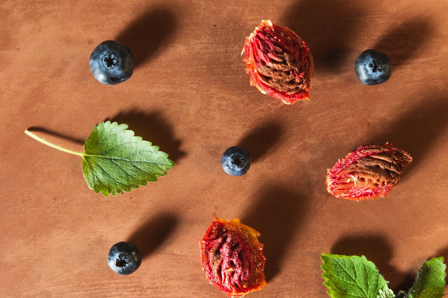 Fresh blueberries and peach pits scattered on a rustic brown wooden surface with basil leaves. b. steele images. food and beverage photos