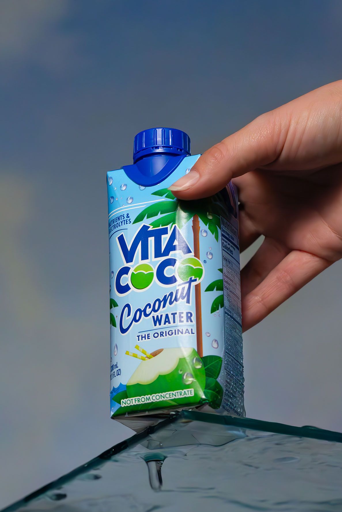 Hand holding a Vita Coco coconut water carton against a light background showing the refreshing beverage packaging. B. Steele Images