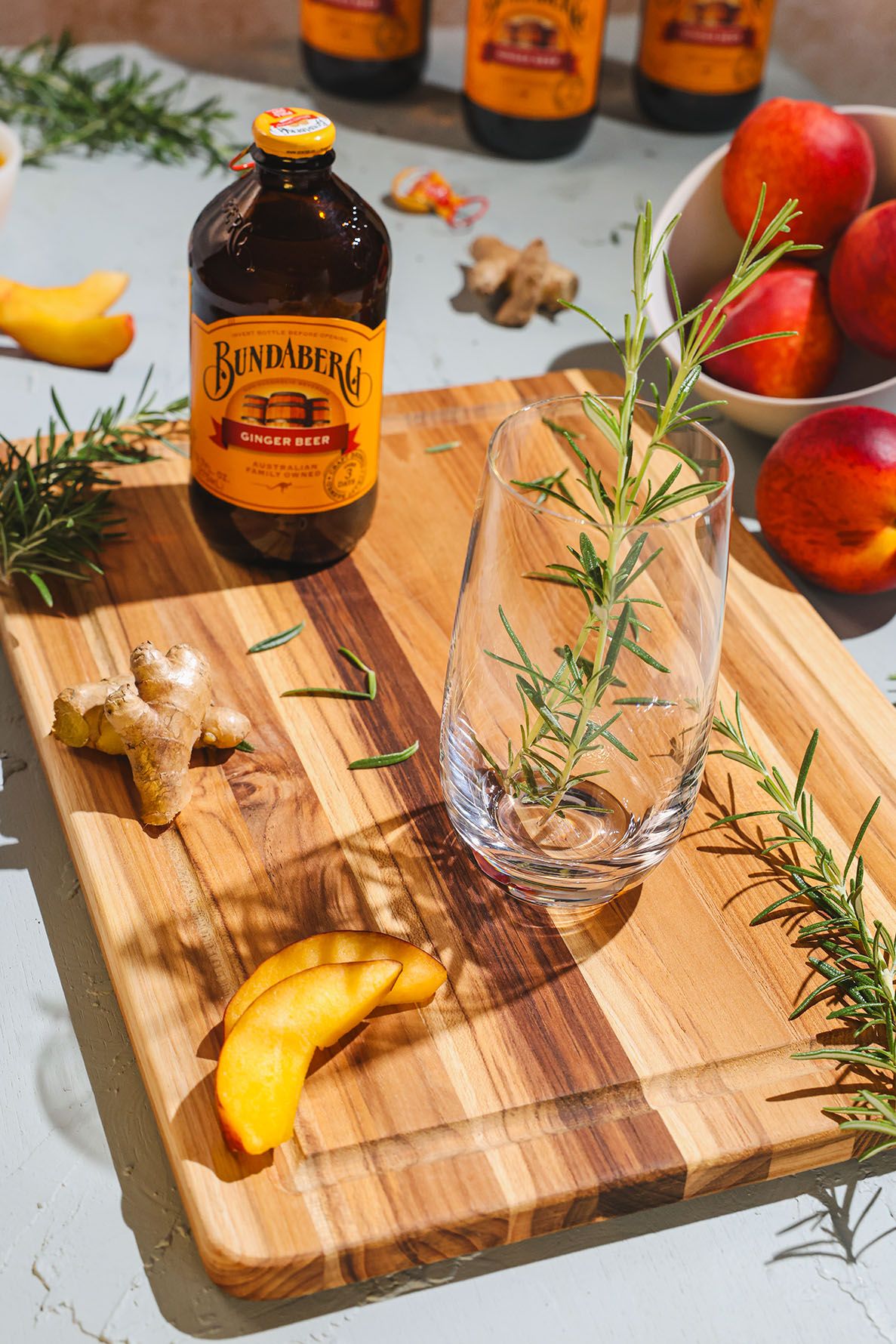 Orange Bundaberg mocktail garnished with fresh rosemary sprig served in a coupe glass on wooden surface with bottle in background. B. Steele