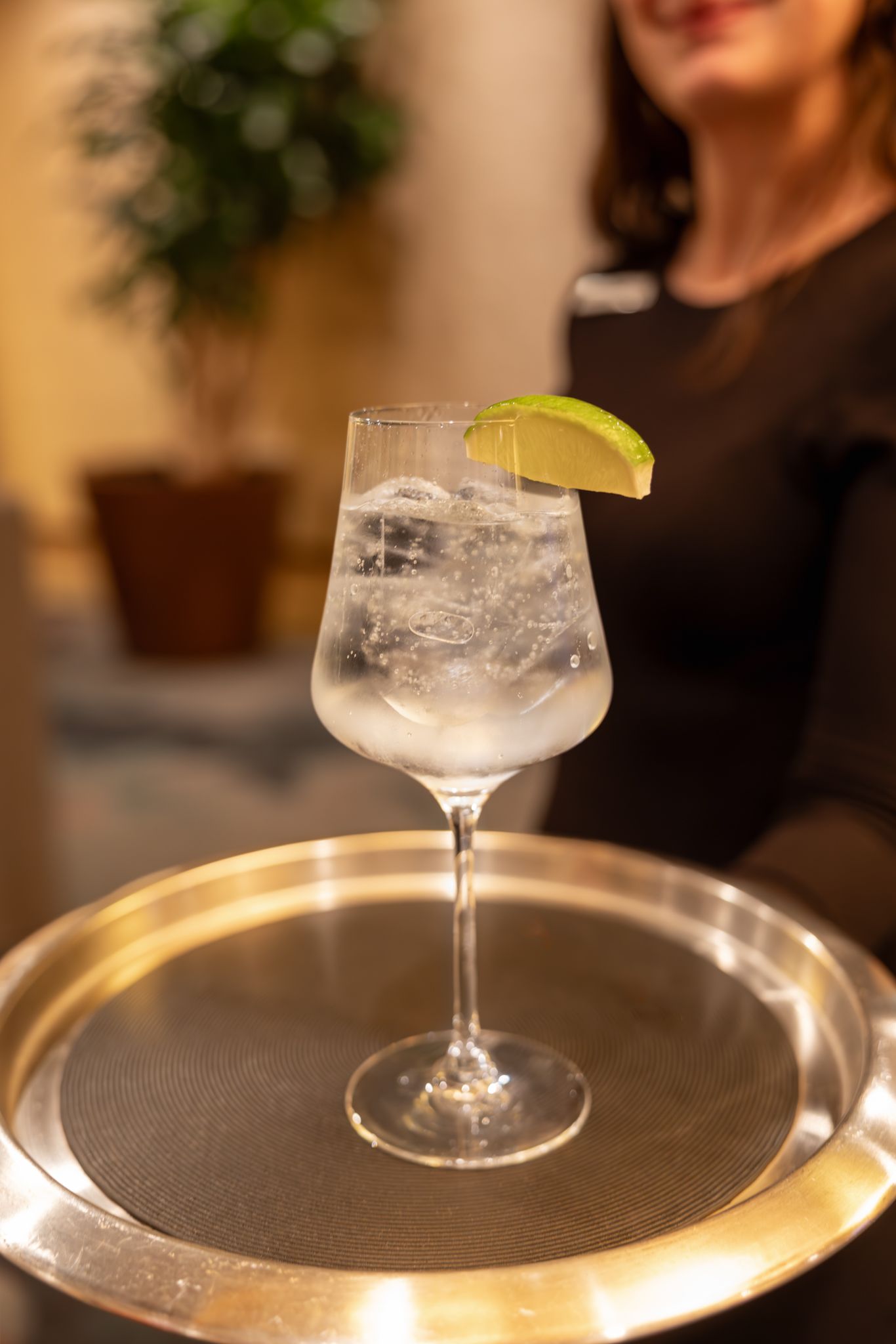 A mocktail glass filled with a clear beverage and garnished with a lime wedge sits on a metallic serving tray. B. Steele Images photography