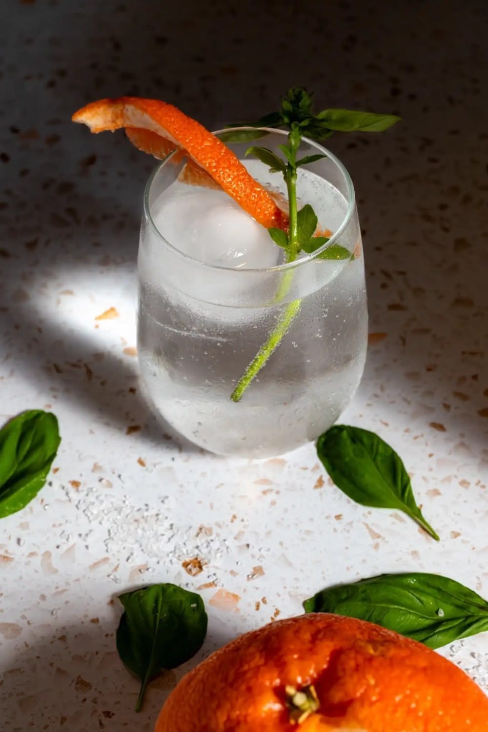 A refreshing mocktail garnished with orange peel and fresh water leaves sits beside a grapefruit. Food styling, B. Steele Images.