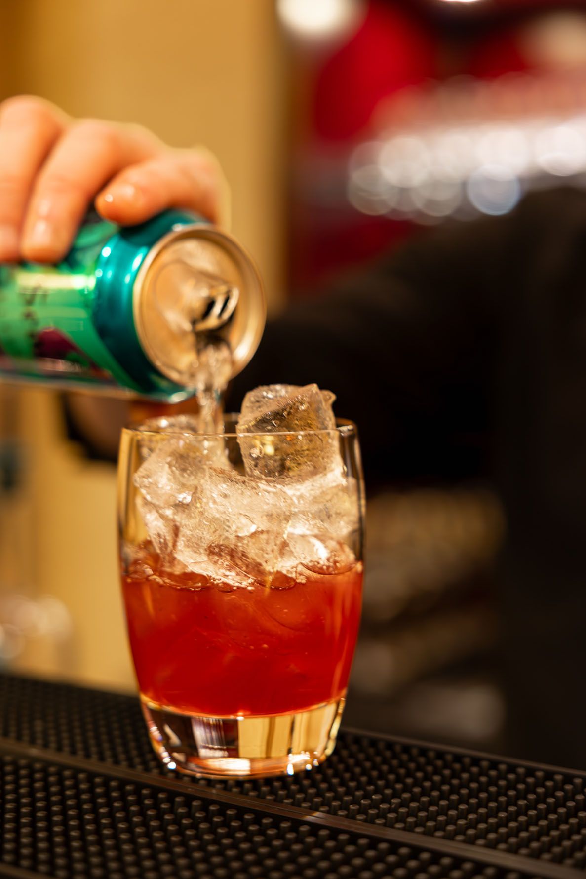 Soda being poured at the bar into a mocktail glass with ice, creating a layered drink effect.