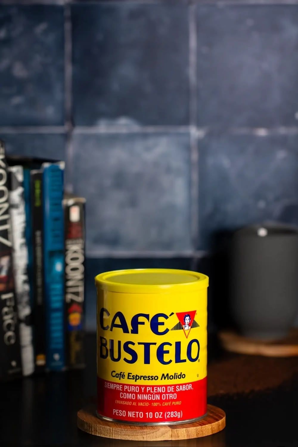 A yellow can of Cafe Bustelo espresso coffee sits on a dark surface with books in the background. Brigit Steele, photography services.