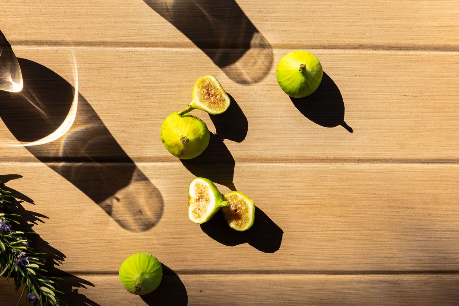 Fresh green figs and a glass jar cast dramatic shadows on a rustic wooden table surface. B. Steele Images, food and beverage photography