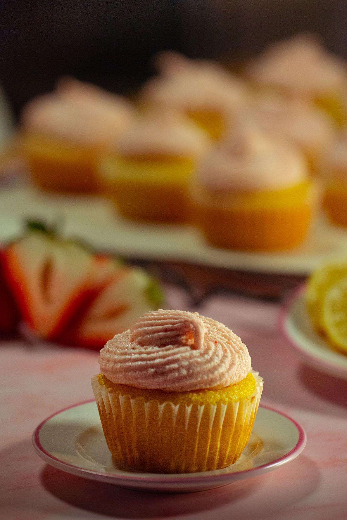 A sequence of identical cupcakes with pink frosting shown from different angles on white plates. B. Steele Images, food photography