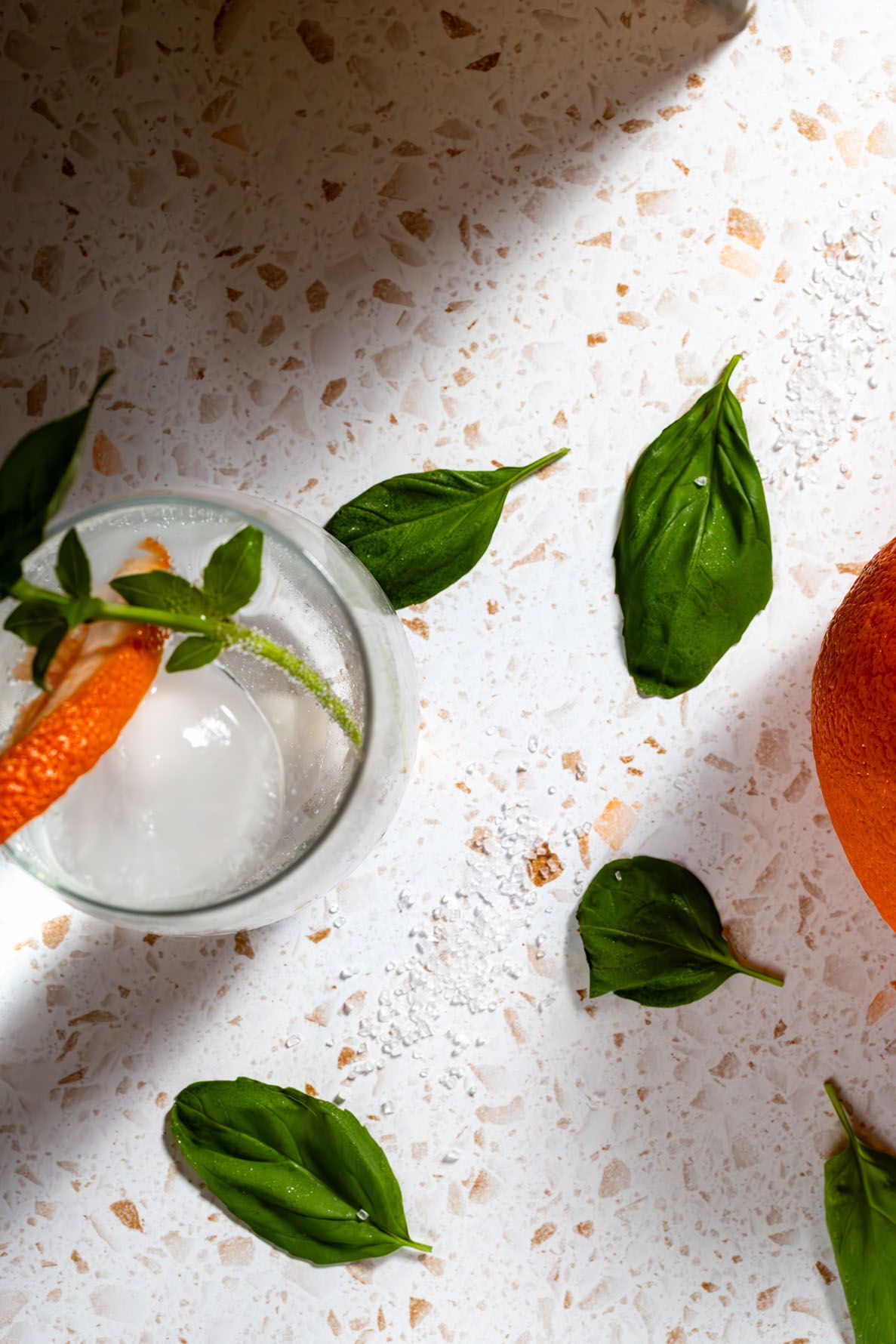 Fresh basil leaves and grapefruit citrus fruit with spritzer arranged on a white textured surface with dramatic lighting and shadows. BSI