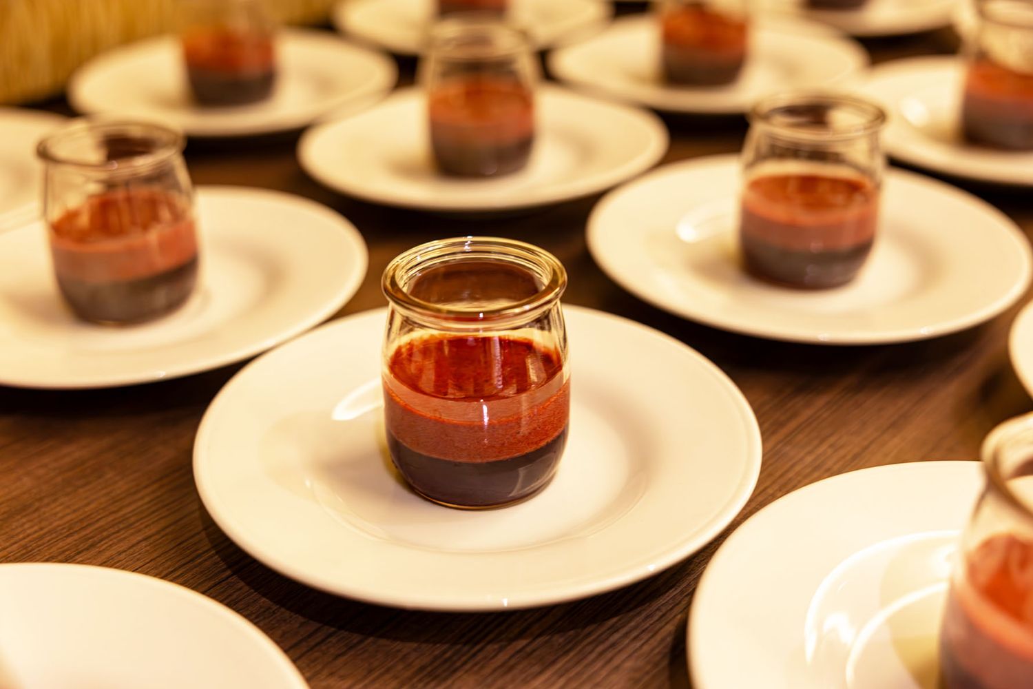 Small glass jars of Elder Wisdom Herbal Tea by Anahata Herbals arranged on white plates on a dark wooden table. B. Steele Images, photograph