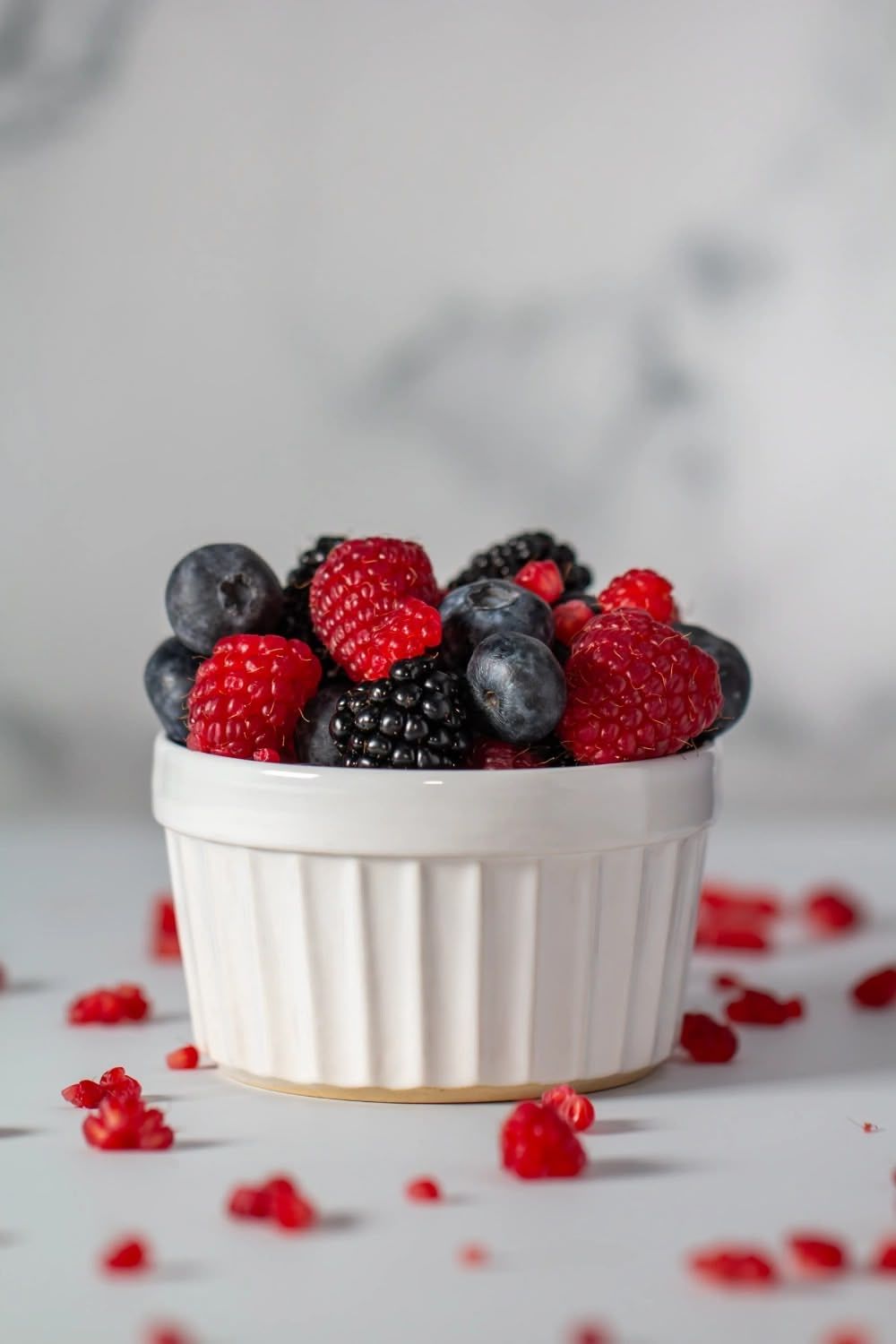 Fresh mixed berries including raspberries, blueberries and blackberries in a white ceramic ramekin on light background. Brigit Steele photo