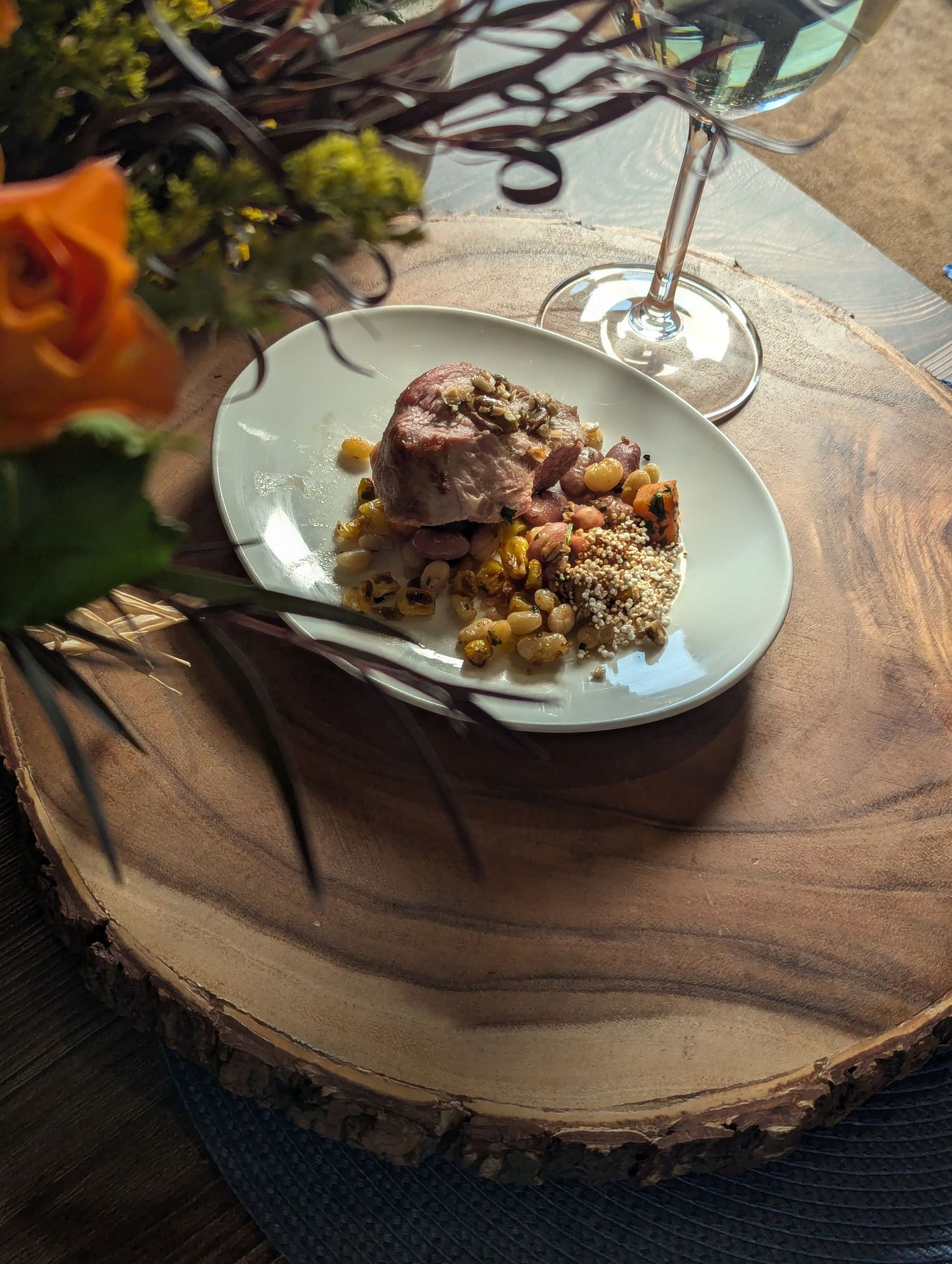 A plated dish of tender meat with grains served on a rustic wooden plank with a wine glass and flowers nearby. B. Steele Images