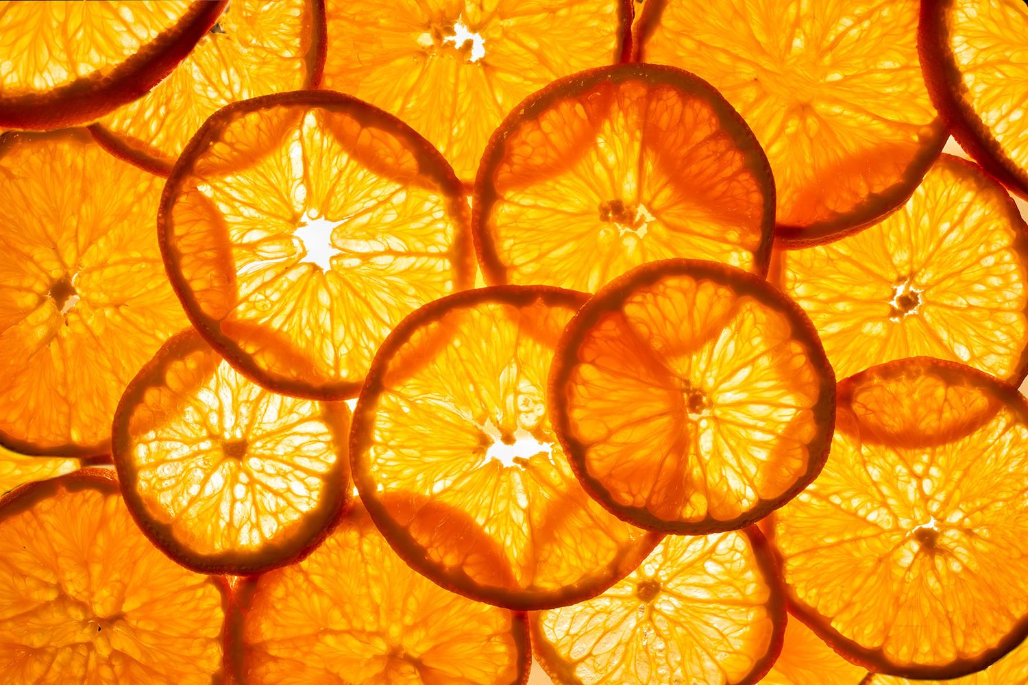 Backlit orange citrus slices arranged in an overlapping pattern creating a vibrant glowing effect. B. Steele Images, food photography