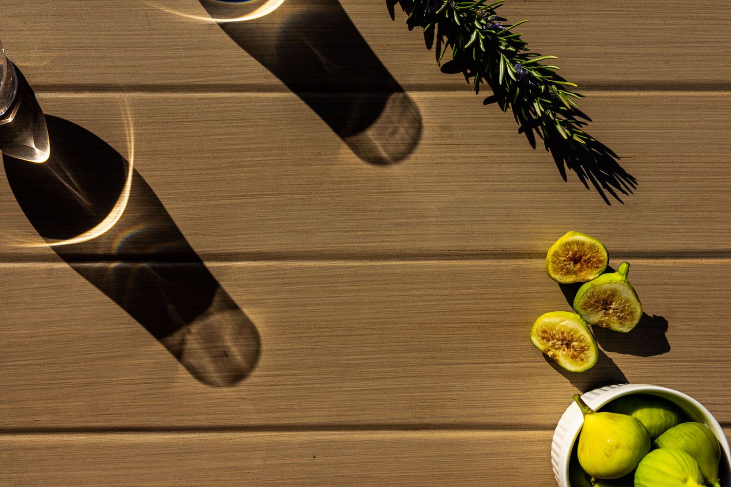Fresh green figs and a glass jar cast dramatic shadows on a rustic wooden table surface. B. Steele Images, food and beverage photography