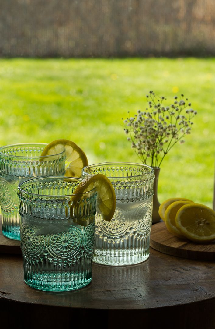 Elegant textured glass tumblers with lemon slices and baby's breath on a wooden surface against a blurred green background.