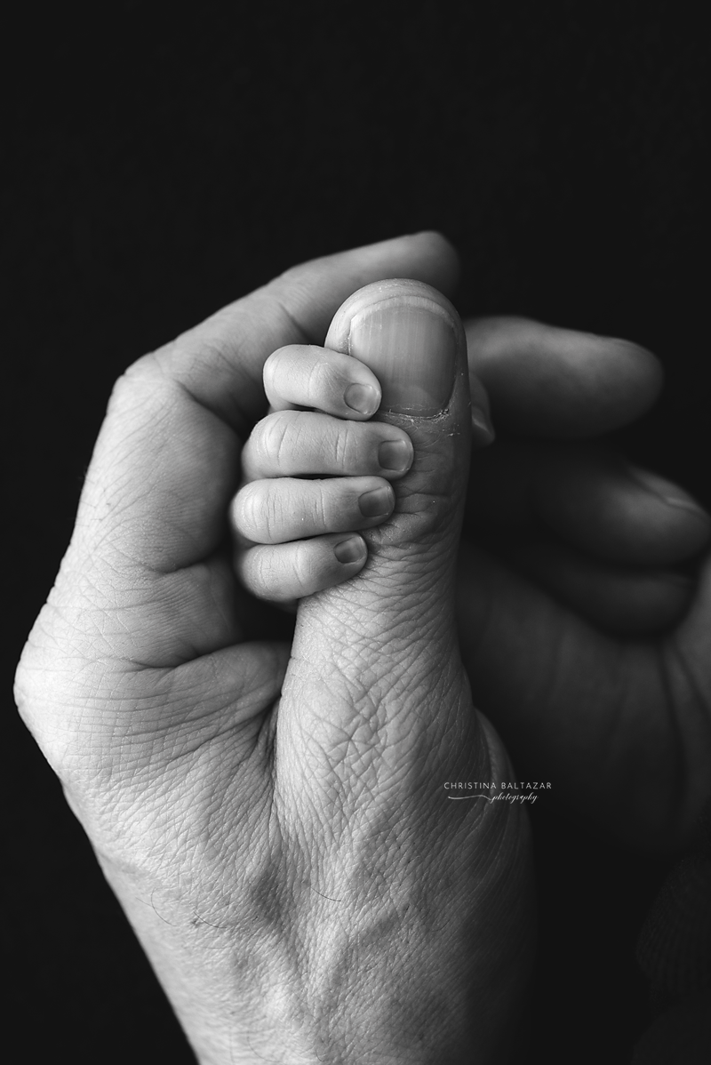 Close-up monochrome image of hands gently clasped together in dramatic lighting.