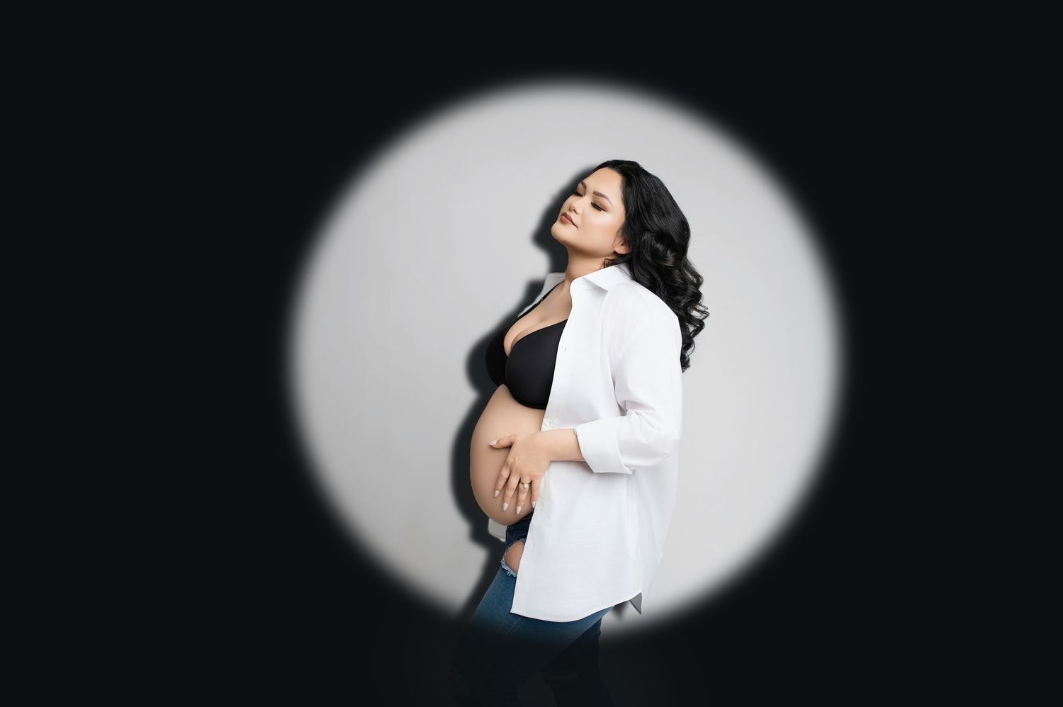 Minimalist spotlight maternity portraits create dramatic oval lighting effects.