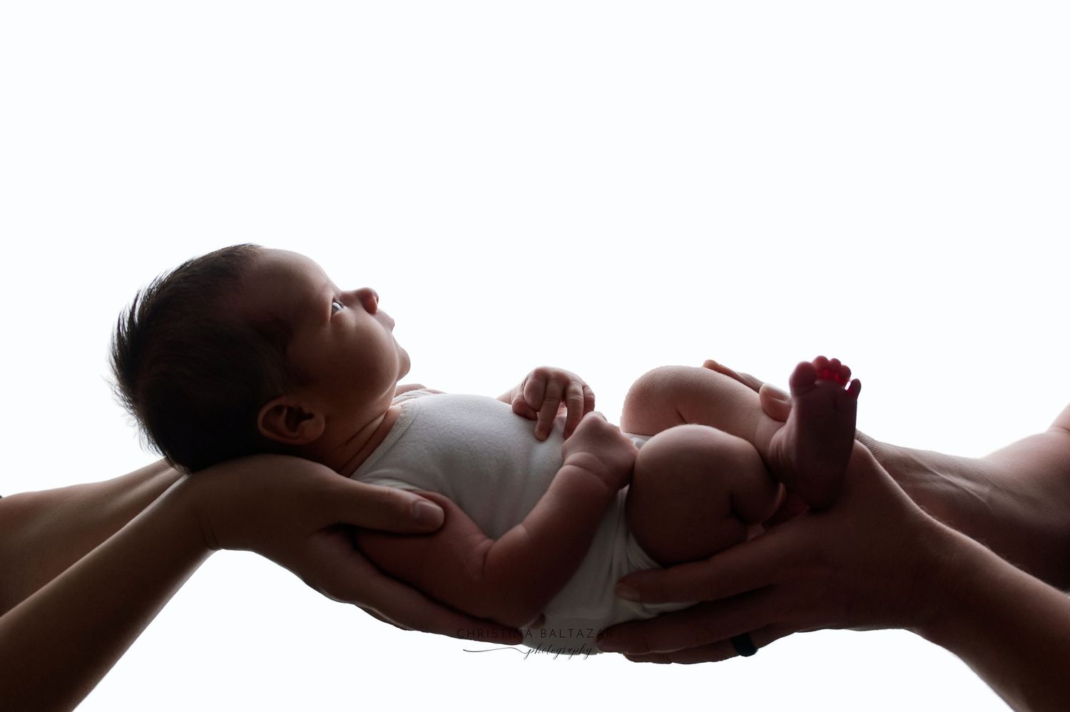 A backlit professional newborn photograph of a baby being delicately held in his parents' hands.  Fresno Newborn Photography