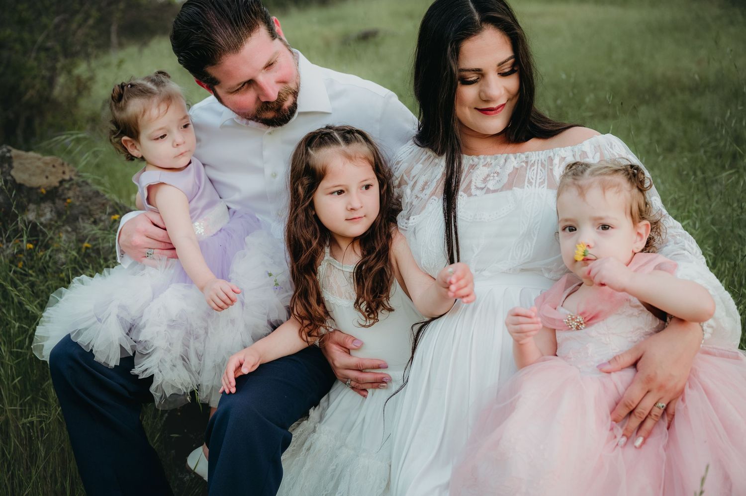 Family wearing white and pink dresses pose together on a grassy hillside. Fresno Family Photography