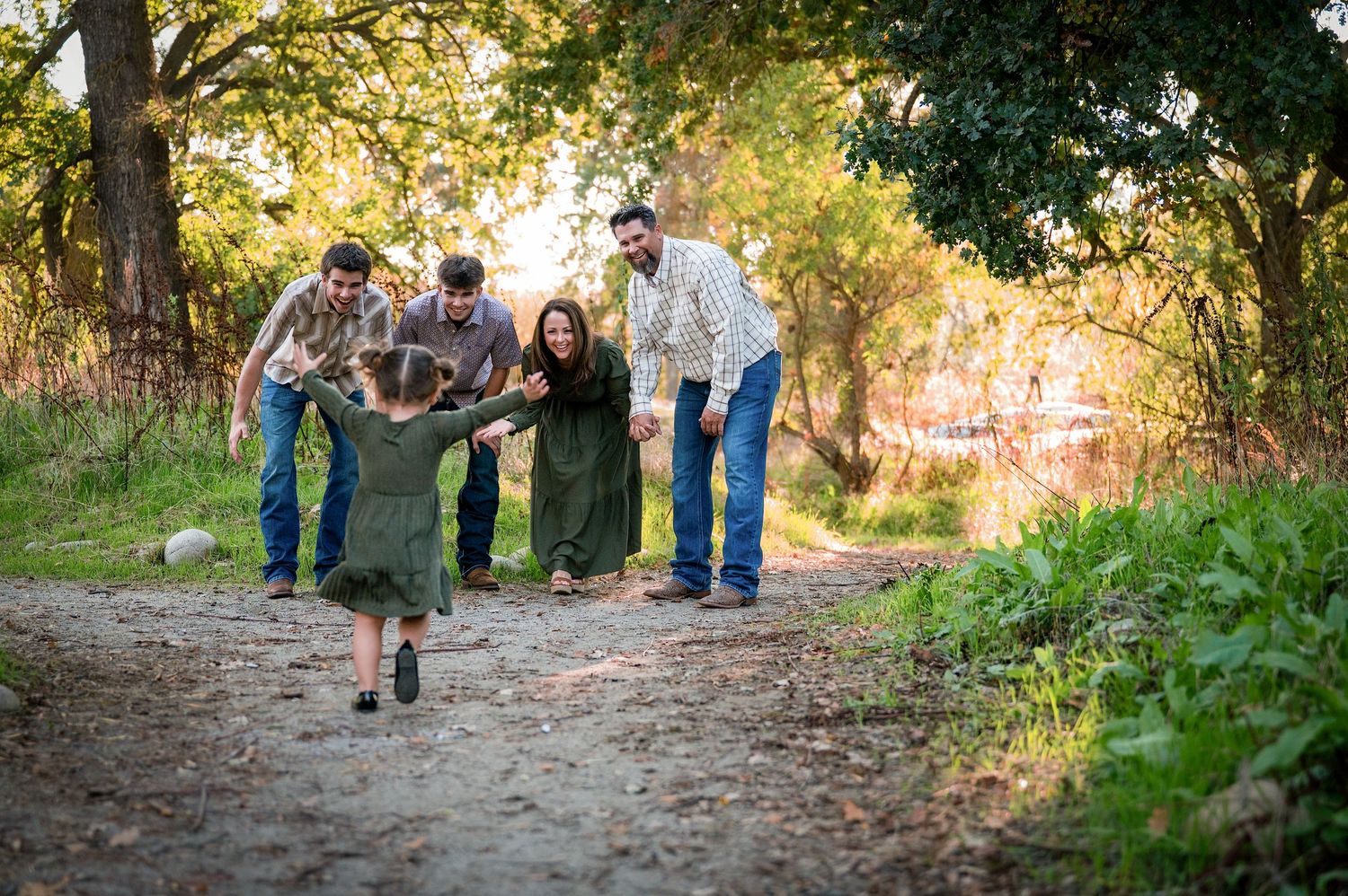Family group walks along wooded trail during golden hour photo session. Hanford Family Photographer