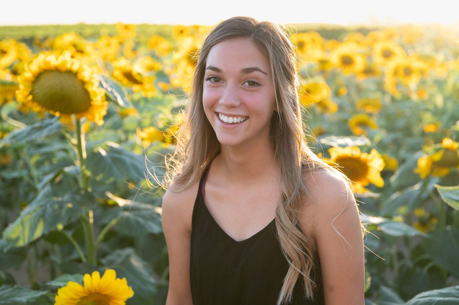 Portrait in a sunflower field with warm evening light and blooming yellow flowers.