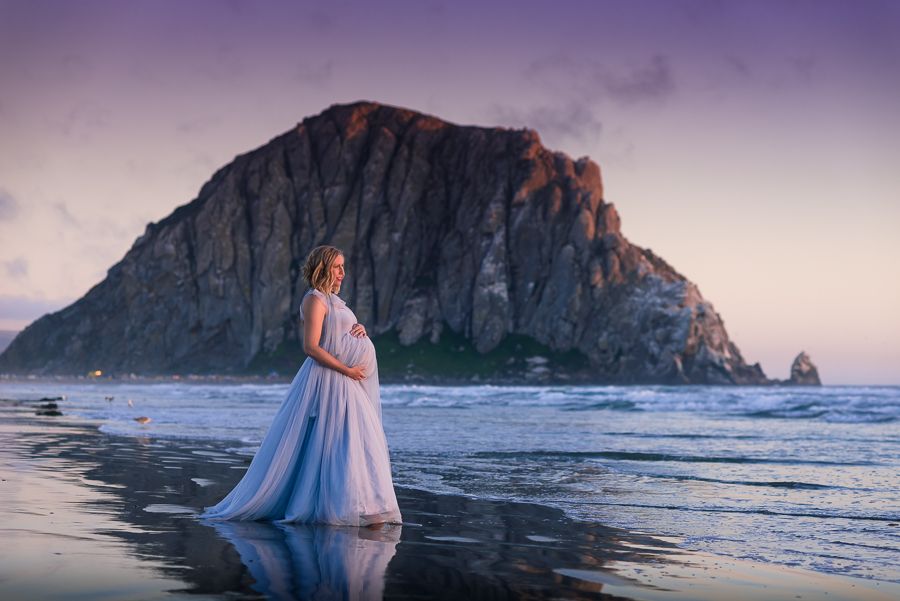 Dreamy sunset maternity portrait at Morro Bay with dramatic cliff backdrop.