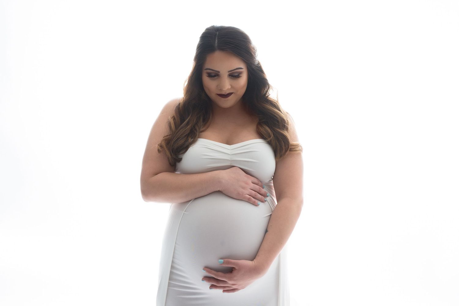 Minimalist maternity portraits in white dress against clean studio background.