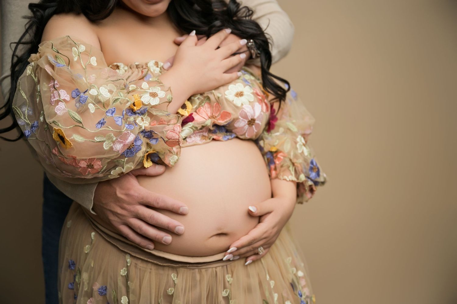 Pregnant woman in floral embroidered tulle dress cradling baby bump during maternity photo session.