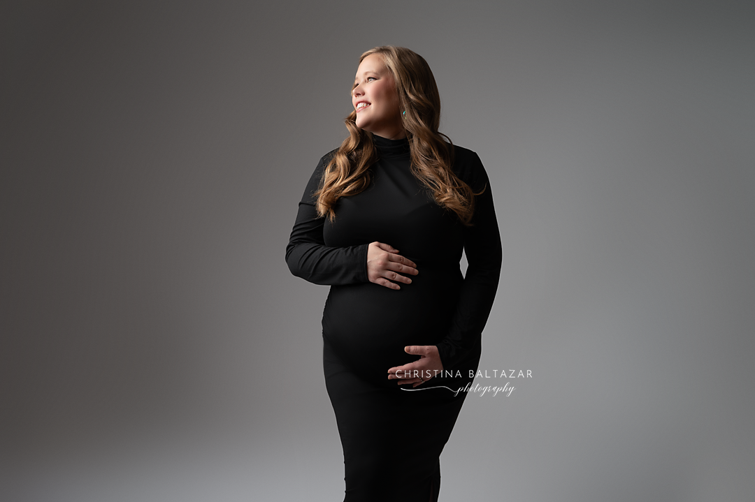 Elegant maternity portrait in black dress against grey background.