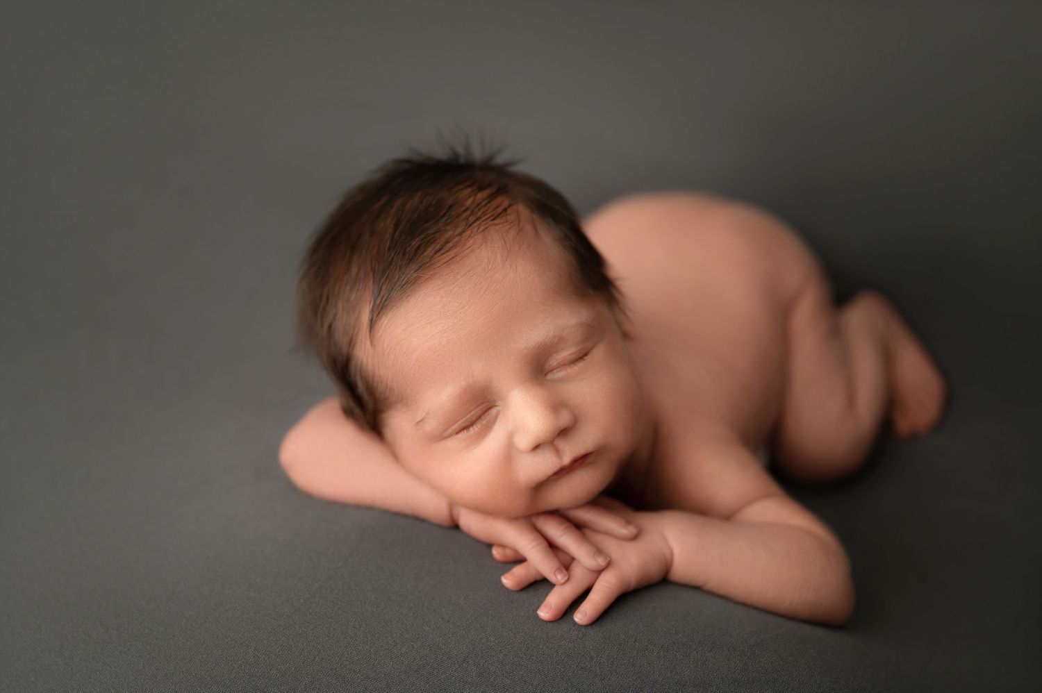 Peaceful newborn sleeping on gray background in artistic portrait pose.