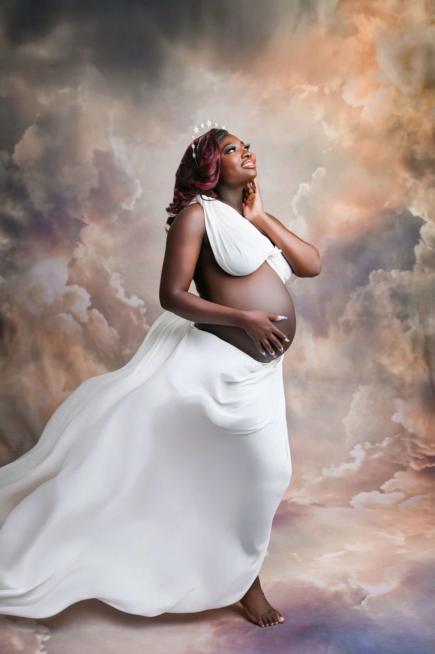 Elegant maternity photography with billowing white dress against dramatic cloudy background.