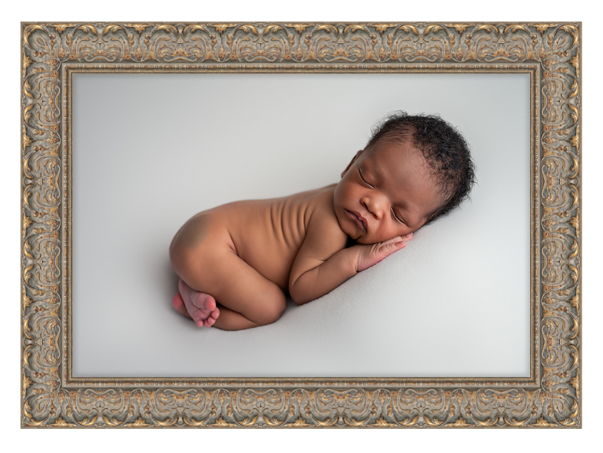 A sleeping newborn baby photographed in black and white with an ornate vintage frame.