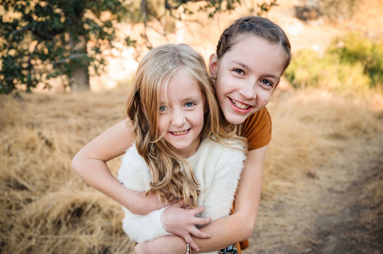 Two friends embrace and laugh together during a golden hour outdoor photoshoot in a grassy field.